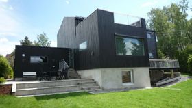 Bilde tatt fra baksiden av huset med betongtrapper og takterrase over tilbygg.