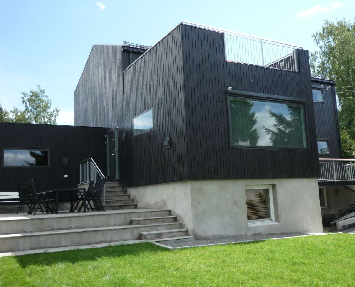 Bilde tatt fra baksiden av huset med betongtrapper og takterrase over tilbygg.