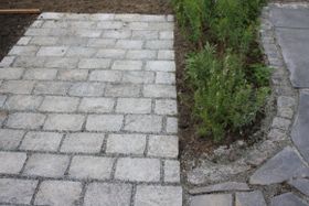 Uteplass i skifer utvidet med stor brostein i granitt. Et blomsterbed er med på å skape skille mellom gammel og ny uteplass.