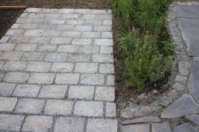 Uteplass i skifer som har blitt utvidet med stor brostein i granitt. Et blomsterbed er med på å skape skille mellom gammel og ny uteplass.