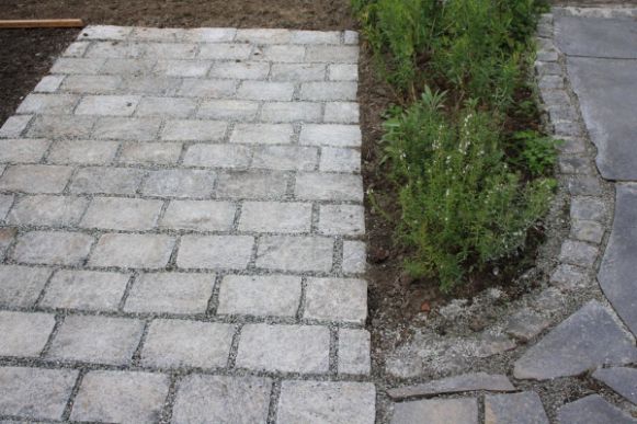 Uteplass i skifer utvidet med stor brostein i granitt. Et blomsterbed er med på å skape skille mellom gammel og ny uteplass.