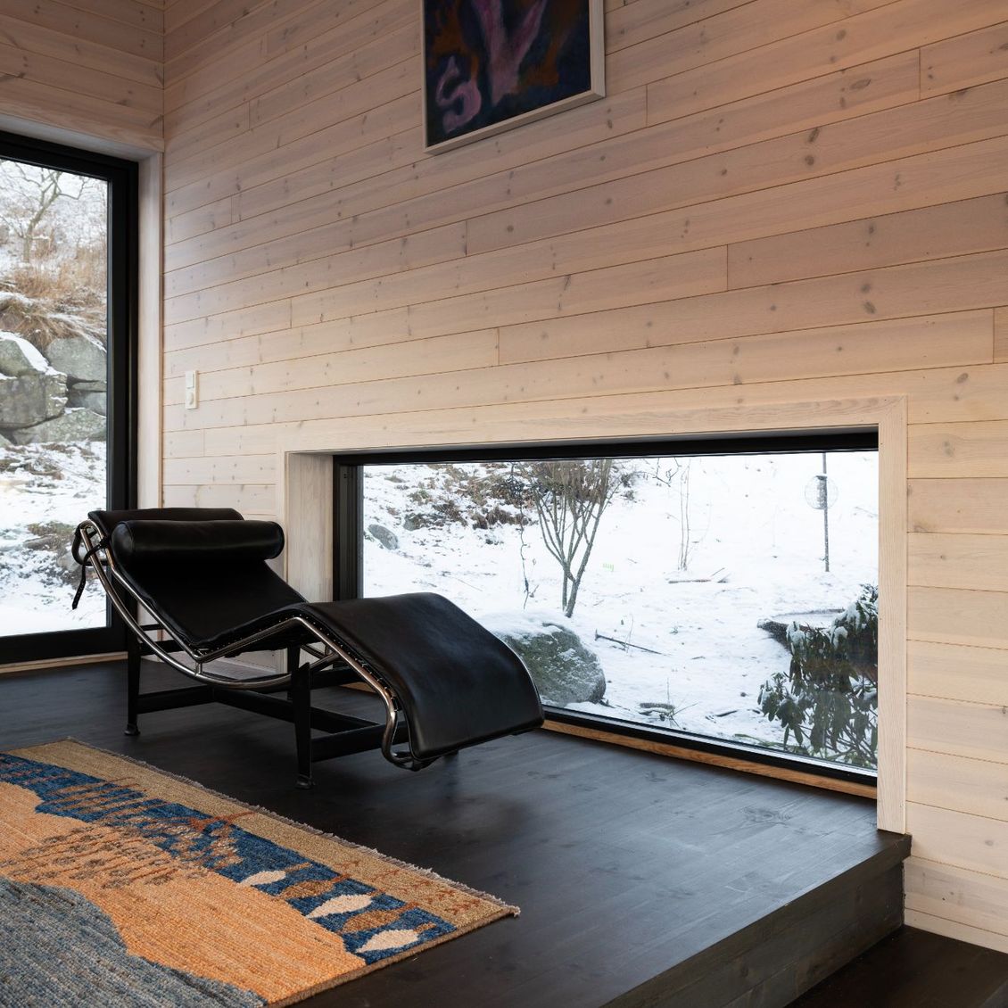 Bilde av stue med 3 vinduer og en daybed/chaiselong foran det ene vinduet som går langs gulvet.